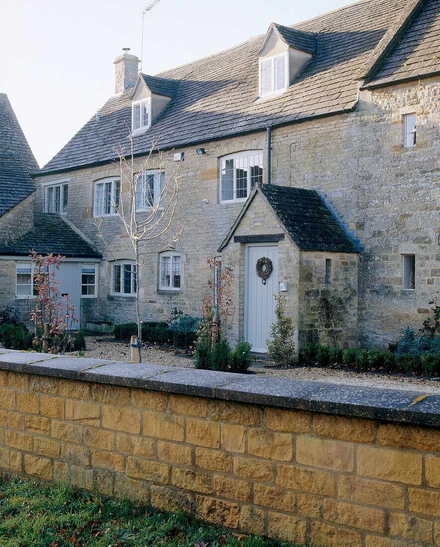 Außenansicht eines traditionellen englischen Steinhauses mit Vorgarten und Eingang, Cotswold, UK