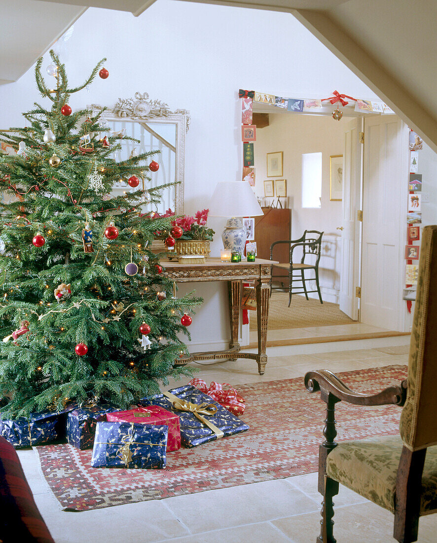 A traditional hallway decorated for Christmas tree with decorations presents stone floor rug side table
