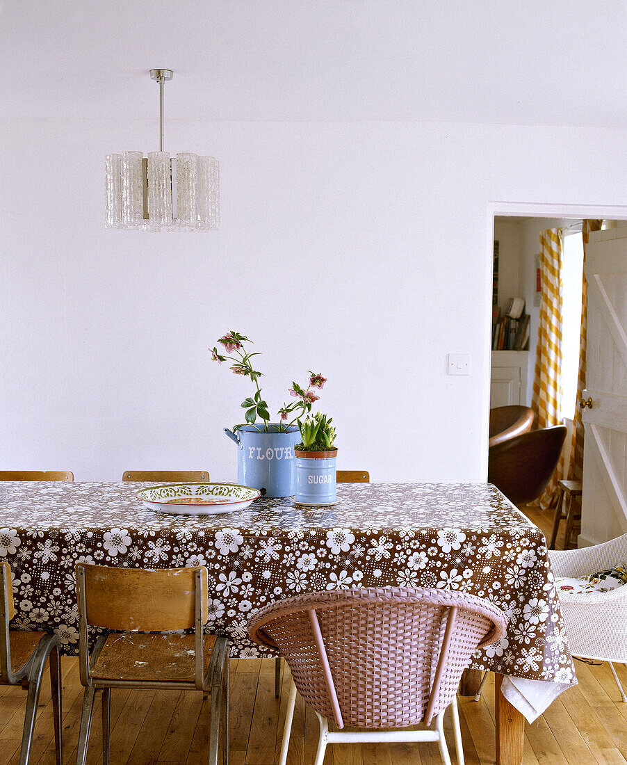 Retro style dining room with floral plastic tablecloth mismatched chairs and perspex hanging light