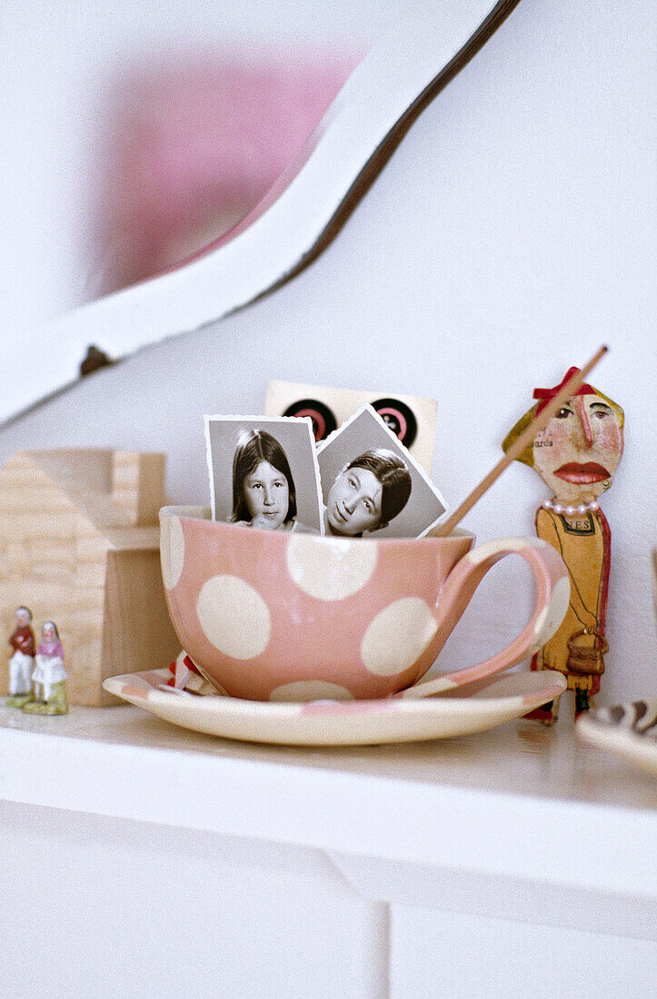 Rosa gepunktete Tasse mit Untertasse aus den fünfziger Jahren und Familienfotos auf dem Kaminsims