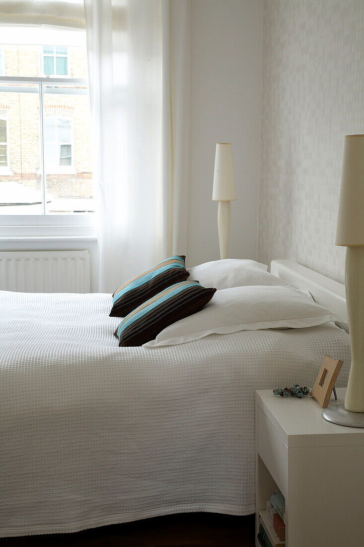 Modernes Schlafzimmer mit weißer Bettwäsche und zwei modernen Lampen auf den Nachttischen an beiden Seiten des Bettes