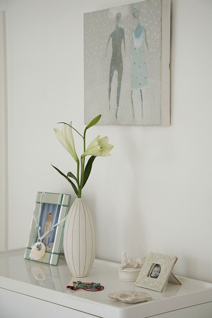 Detail of ornaments white vase of flowers and several framed pictures below a painting