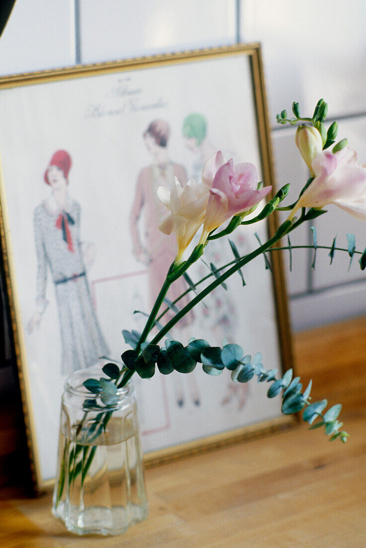 Close up of a glass vase of flowers in front of a framed drawing