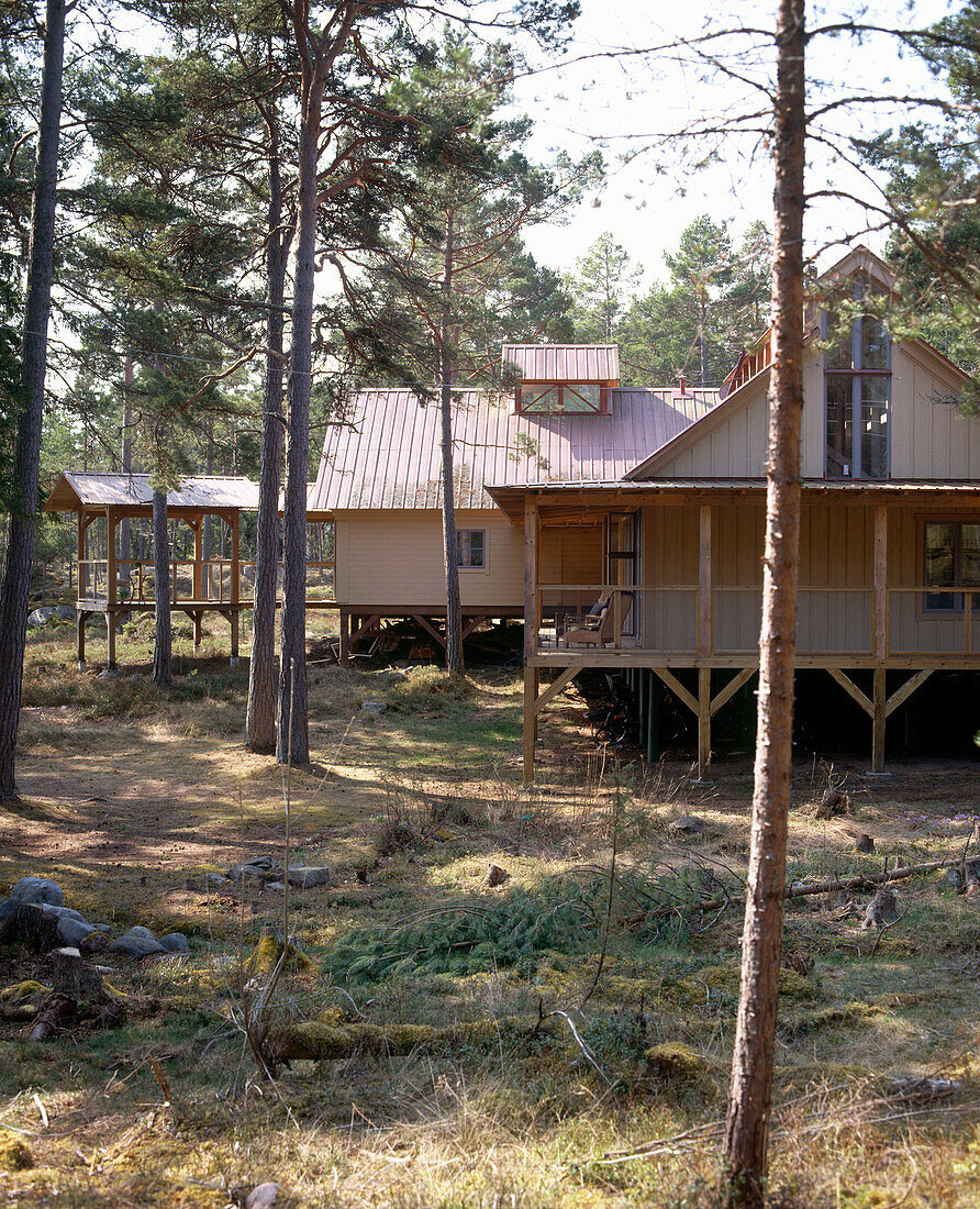 Außenansicht eines traditionellen Holzhauses, das auf Holzbeinen steht und von Bäumen umgeben ist