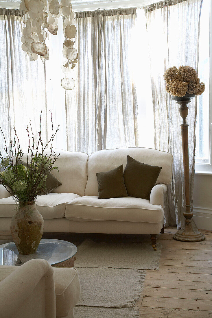 Blumenarrangement auf dem Couchtisch gegenüber dem Sofa vor einem Fenster mit geschlossenem Vorhang