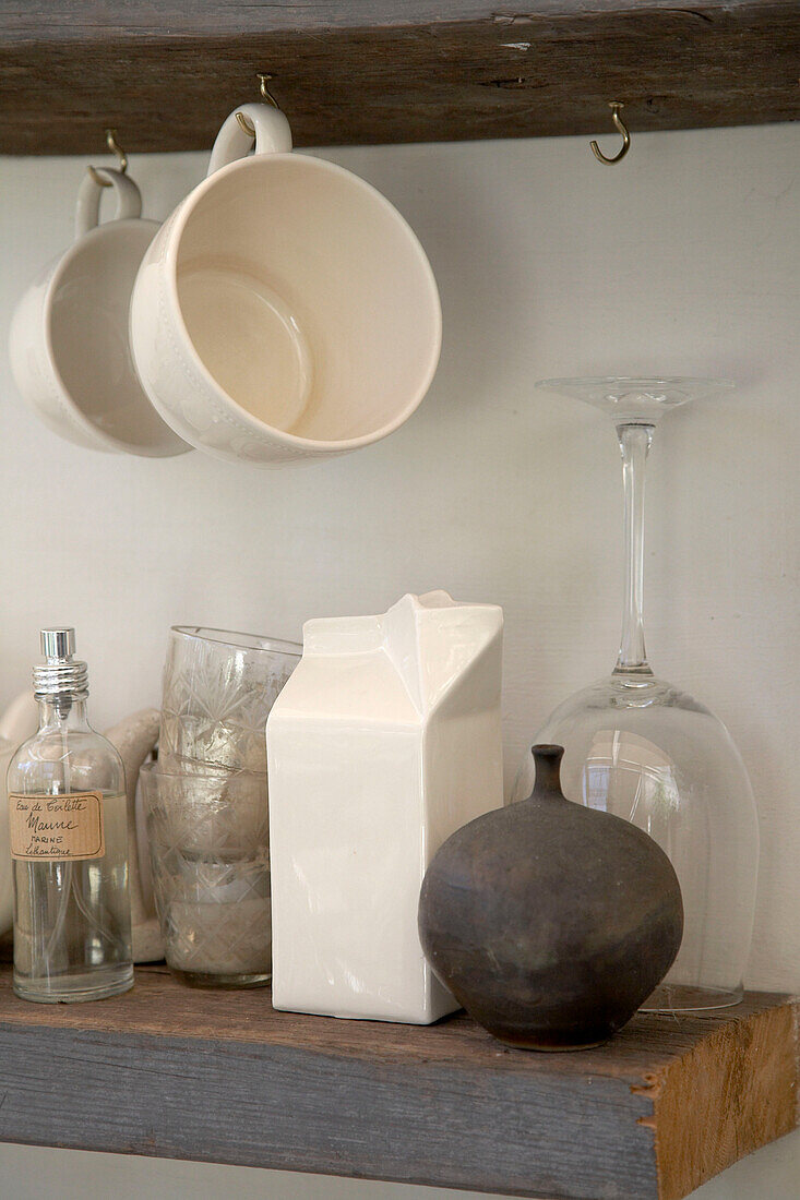 Large cups hanging from hooks above glassware items on wooden shelf