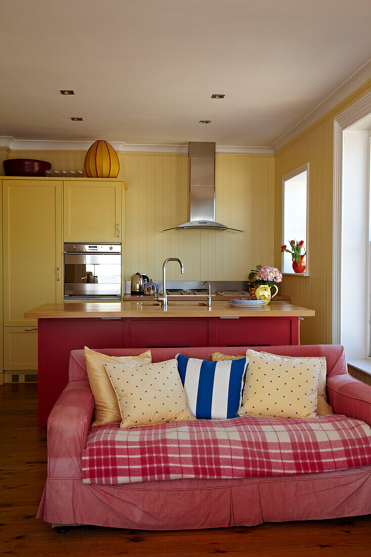 Pinkfarbenes Sofa in offener Küche mit Kücheninsel in Cromer Strandhaus, Norfolk, England, UK