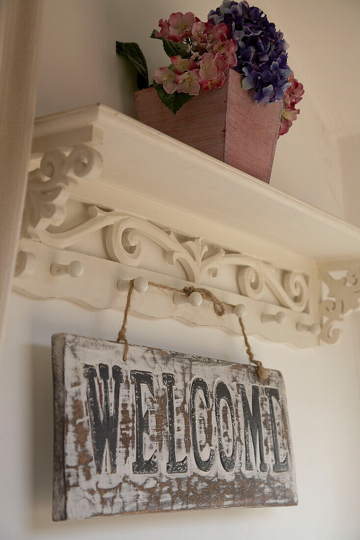 Detail of decorative shelve with planted flowers and welcoming wooden plate