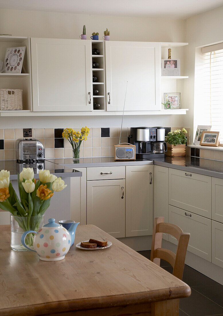 A modern country style kitchen with white units and wooden breakfast table with tulips in a vase