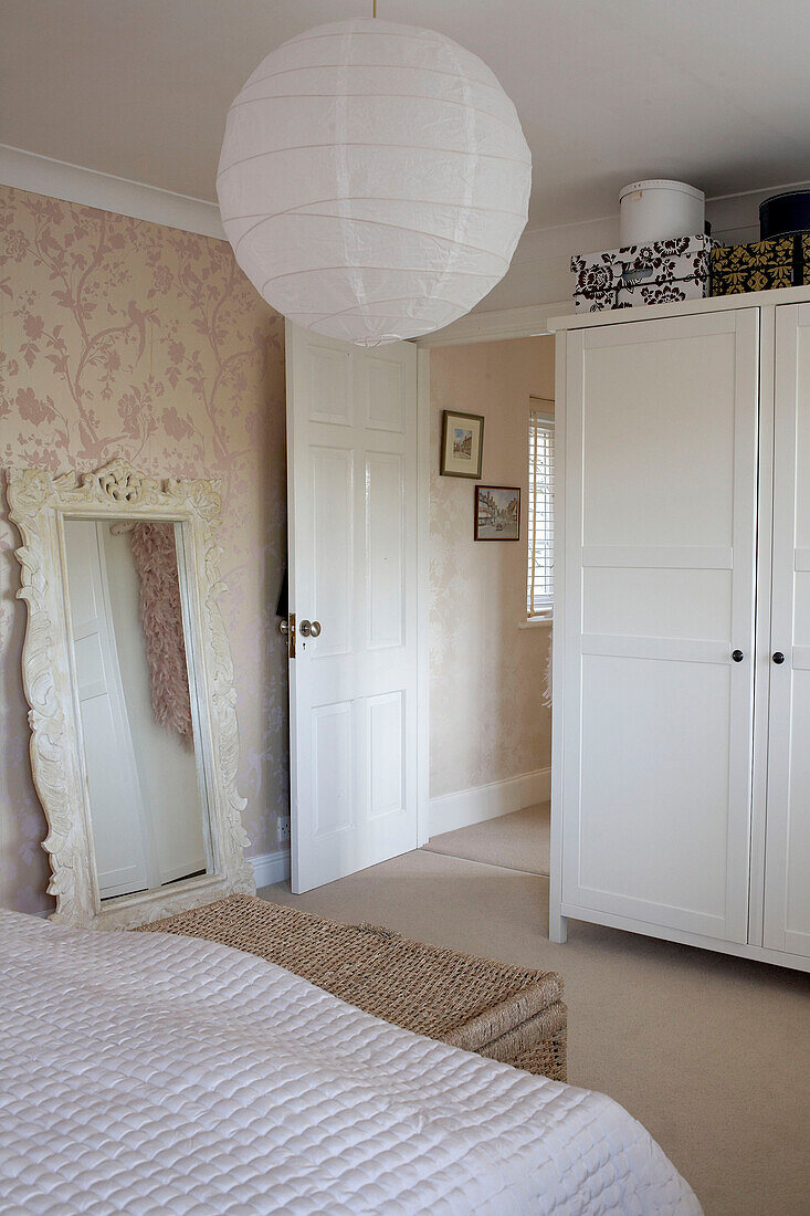 A detail of traditional country style bedroom with framed wall mirror white wooden wardrobe done in neutral colours
