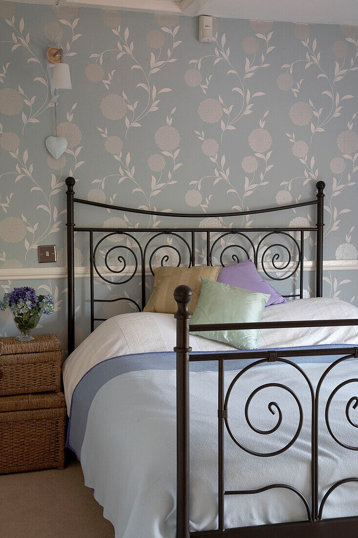 A traditional bedroom with an iron bed with blue linen wallpaper and wooden bedside table