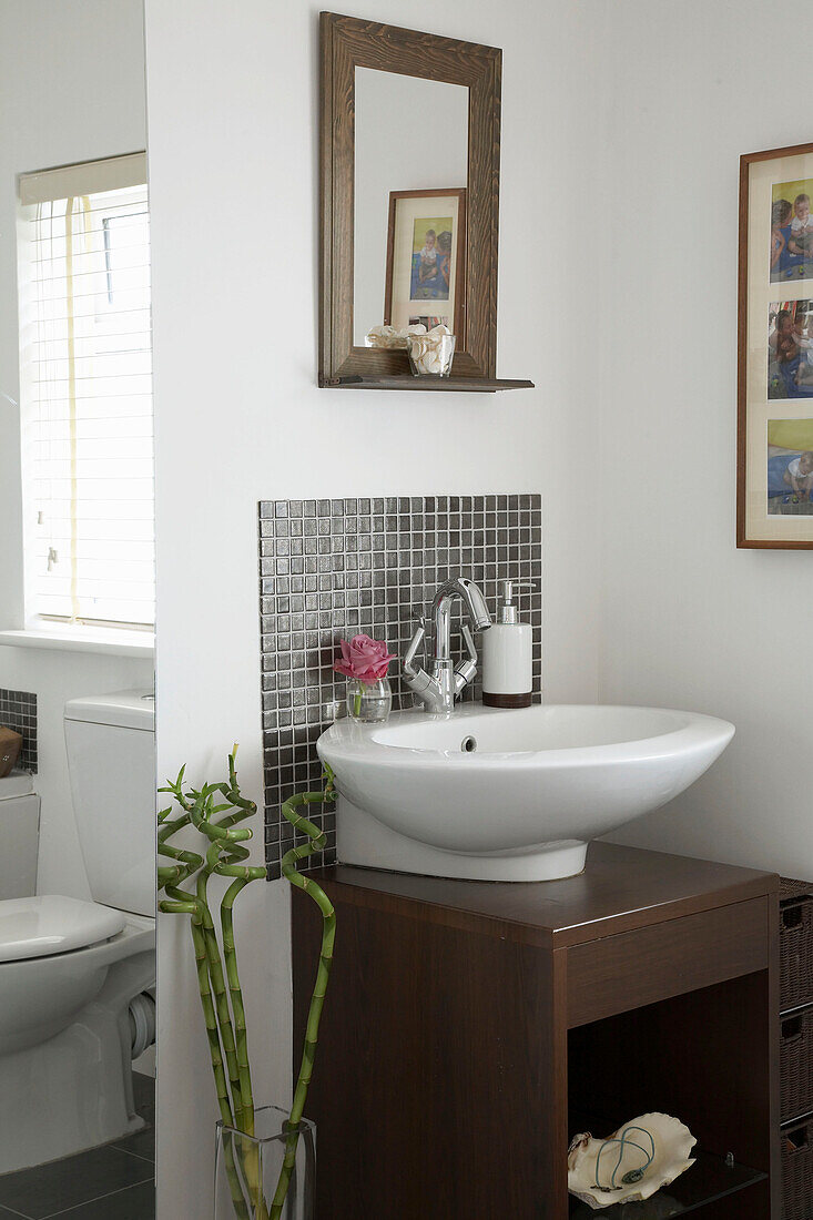 Detail eines modernen Badezimmers mit weißem Waschbecken auf einem Holzsockel und gerahmtem Spiegel darüber