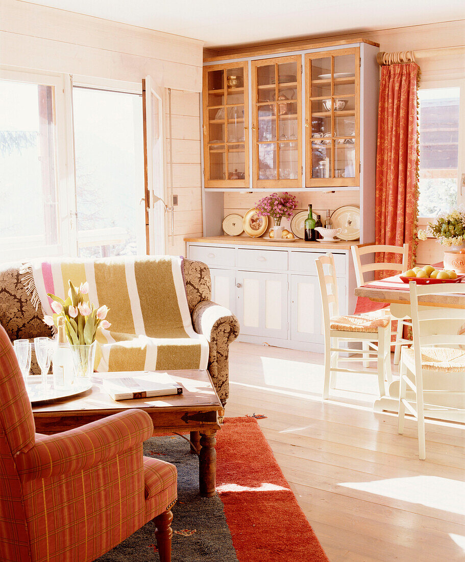 Wohnzimmer im Landhausstil mit Essecke, Holzvertäfelung, Polstersesse,l Couchtisch, Kommode, Holzboden und rotem Teppich