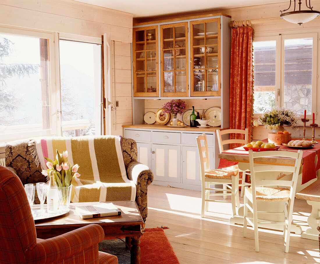 Wohnzimmer im Landhausstil mit Essecke, Holzvertäfelung, Polstersessel, Couchtisch, Kommode, Holzboden und rotem Teppich