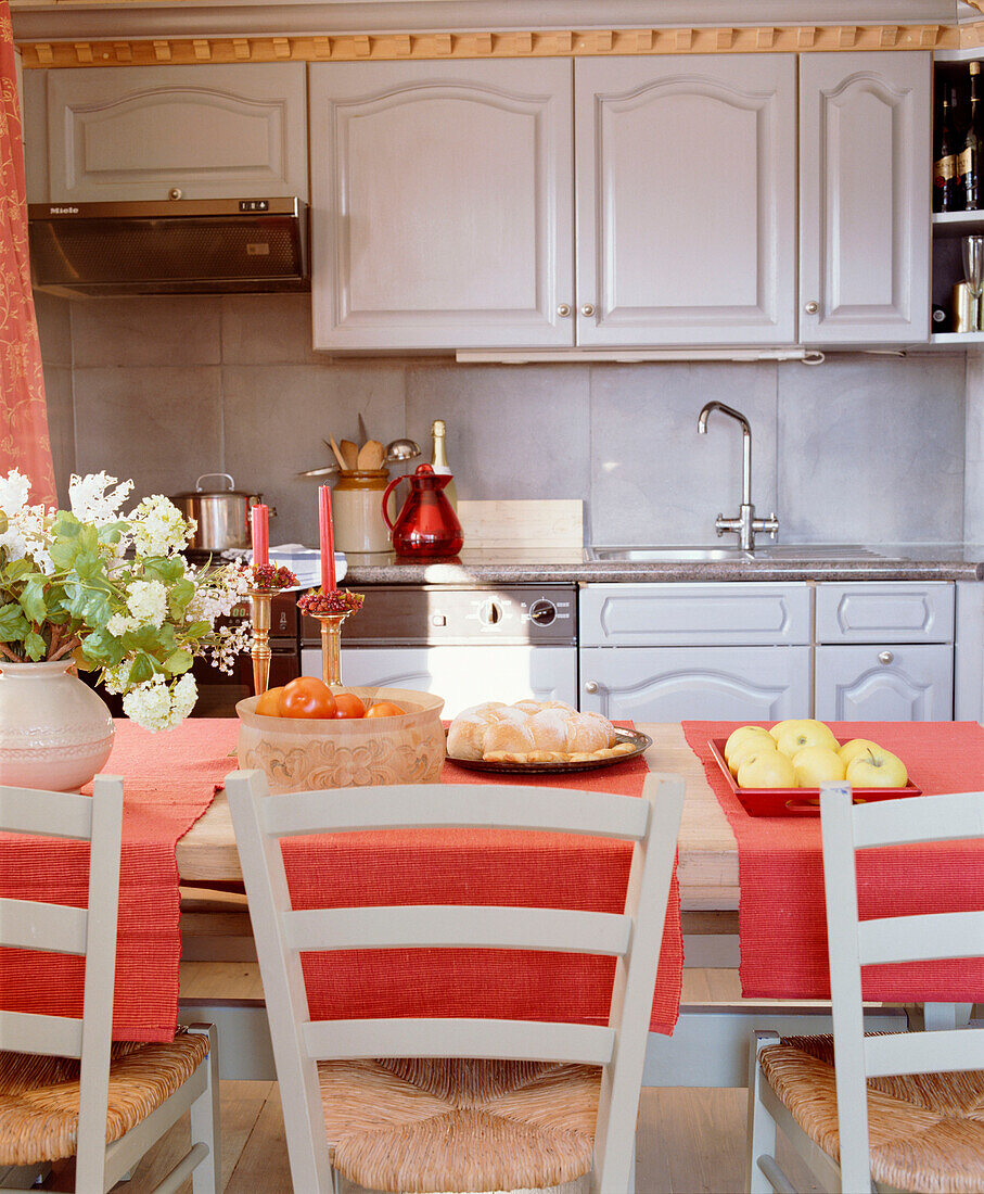 Offene Küche im Landhausstil mit Essecke, Holztisch, Stühlen mit Binsensitzen, bemalten Schränken und Tischläufer