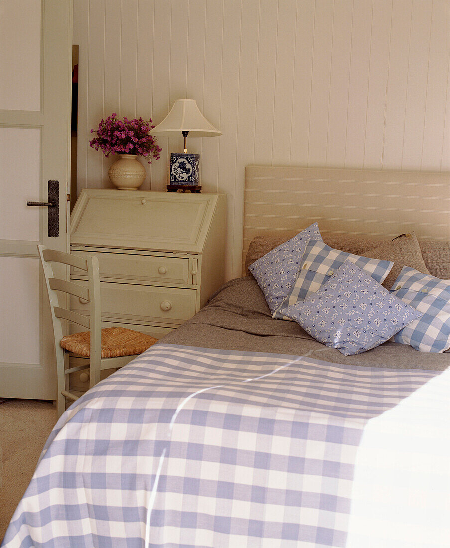 A detail of a country style bedroom double bed with upholstered headboard painted bureau lamp chair with rush seat
