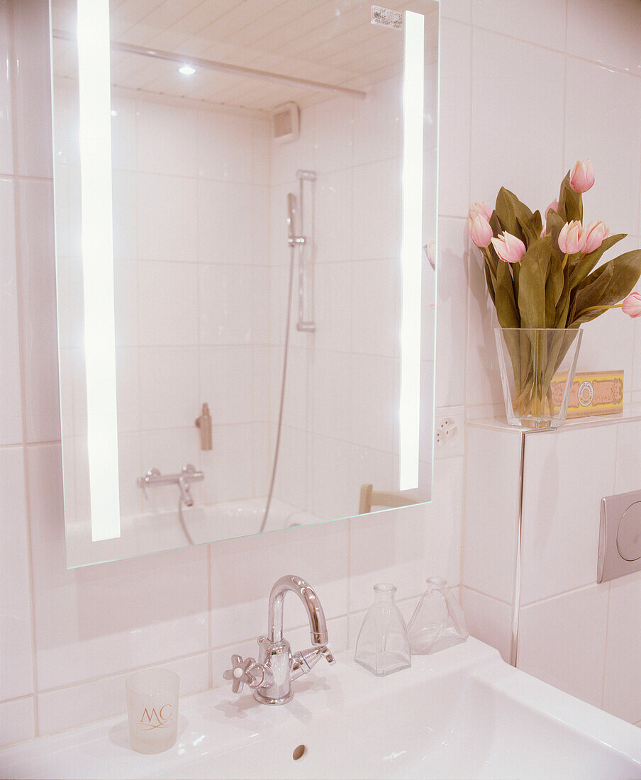 Modernes Badezimmers weiß gefliesten Wänden, wandmontiertem Waschbecken und beleuchtetem Spiegel