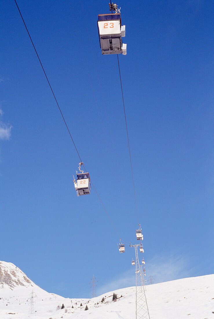 View from below of cable cars suspended over snow covered mountains