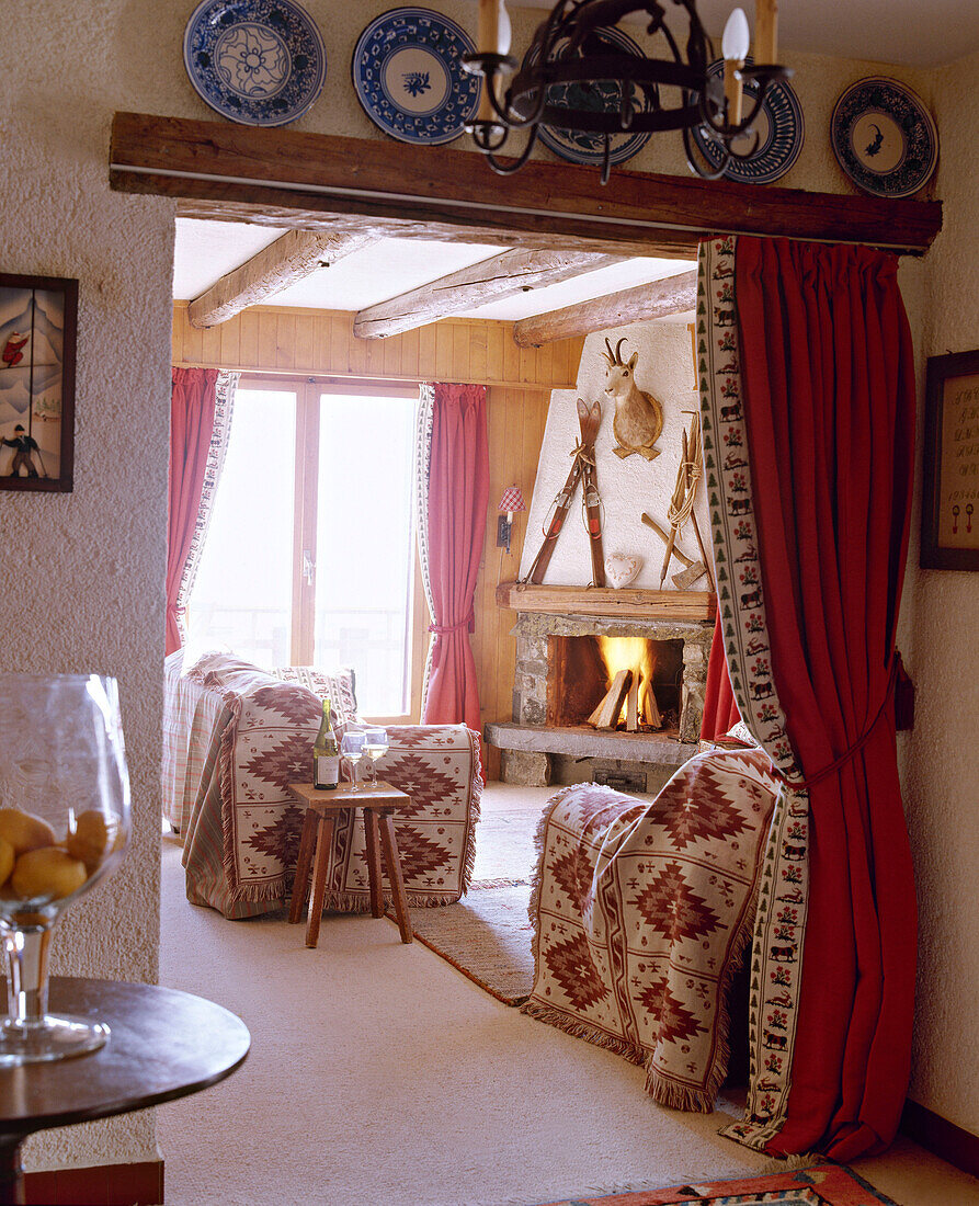 Blick durch die Tür zum Wohnzimmer mit Steinkamin, Balkendecke und Sofas mit Überwürfen