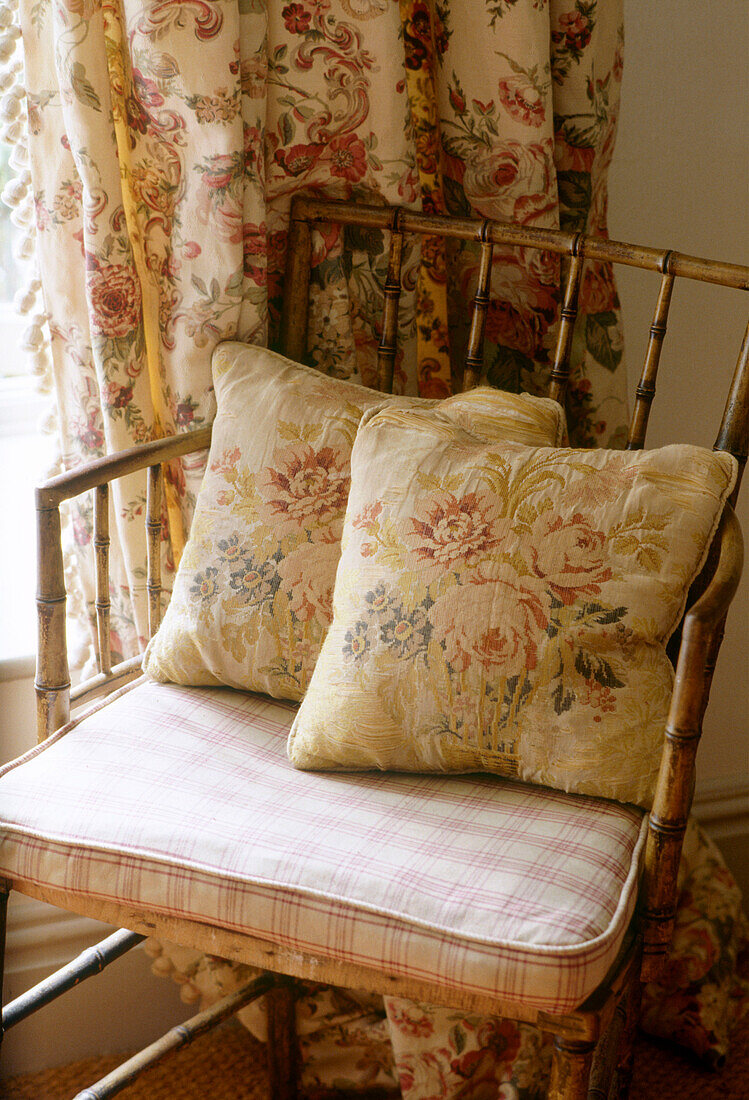 Blumenmuster-Kissen auf Sessel aus Rohrgeflecht im Landhausstil
