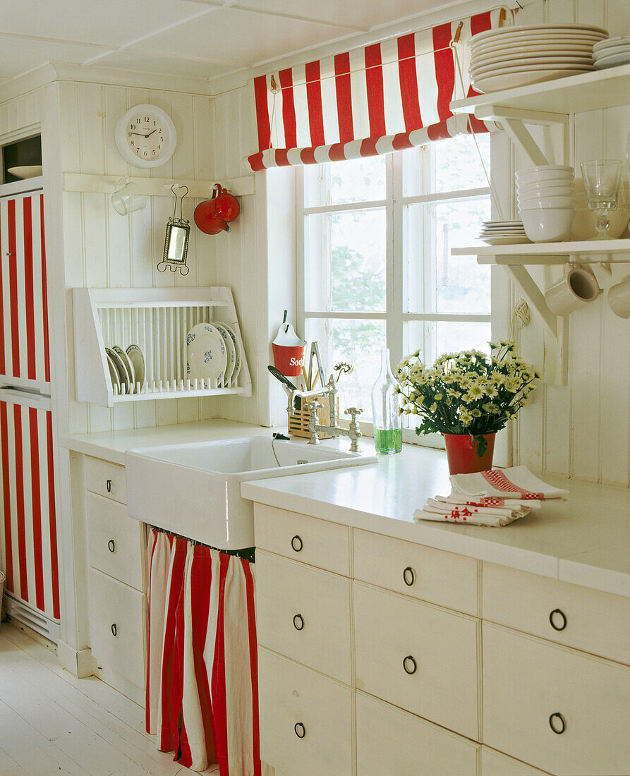 A country kitchen in neutral colours Belfast sink painted units red and white striped blind and curtain shelving tableware