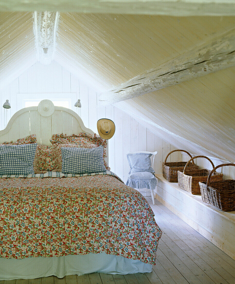 Ein Schlafzimmer im Landhausstil mit Holzboden, Holzbalken, Doppelbett mit geblümtem Bettbezug und Weidenkörben