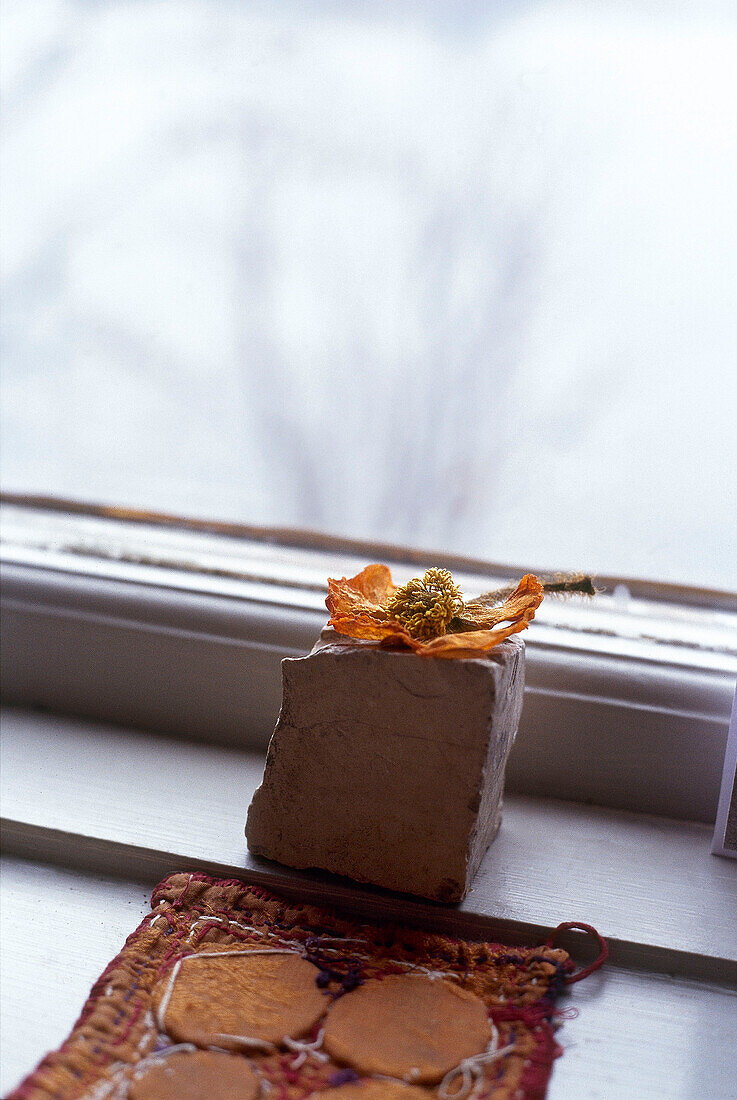 Handgefertigter Untersetzer aus getrockneten Blumen und Ziegelsteinen auf der Fensterbank