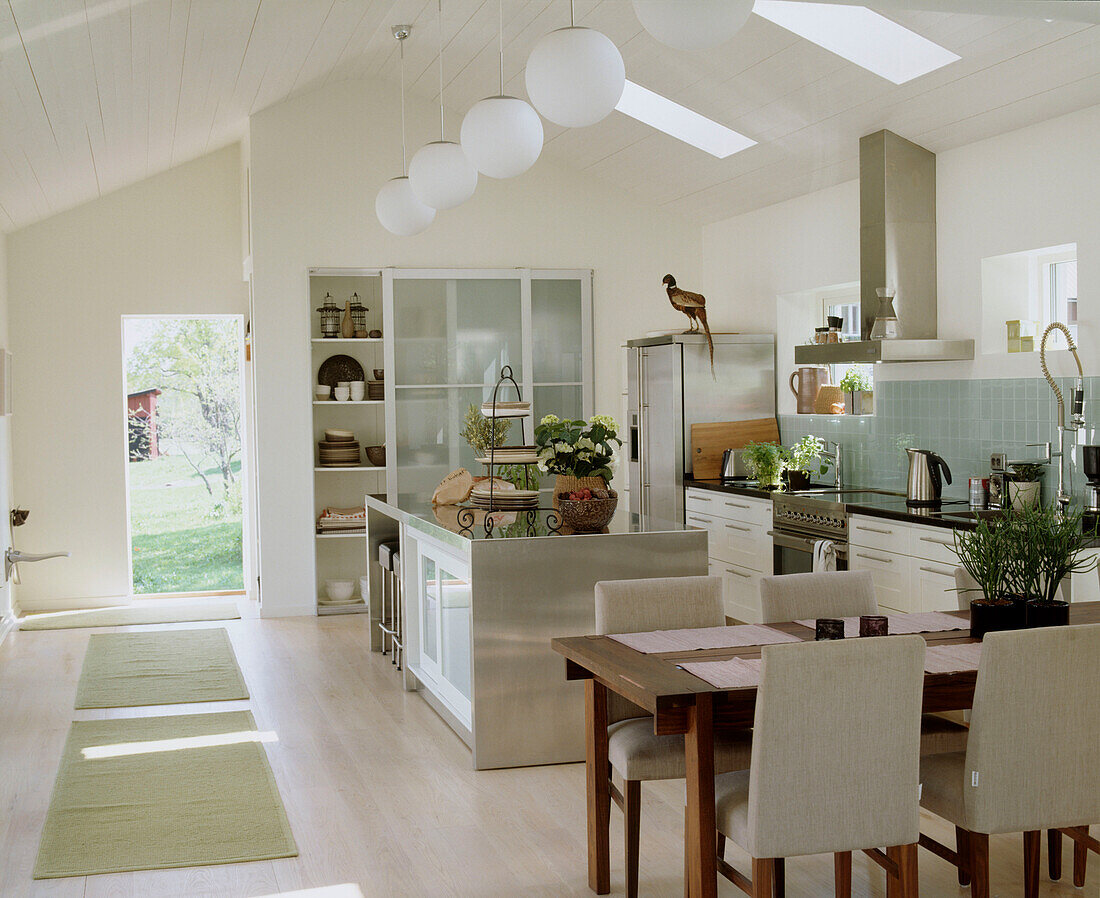 A modern open plan kitchen dinning room in country style with wooden dining table and chairs white kitchen units and an open door leading outside
