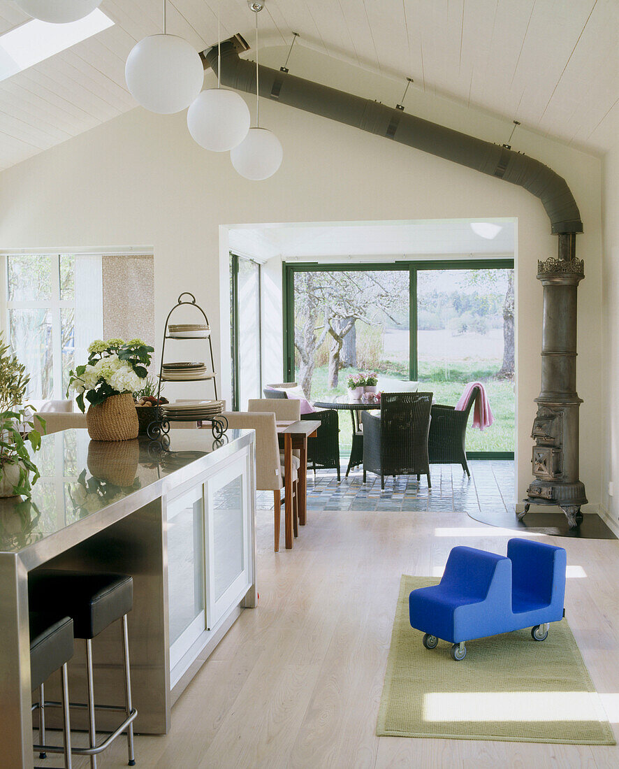A modern open plan kitchen dinning room in country style with a table and chairs in breakfast area by big windows traditional wood burner in a corner