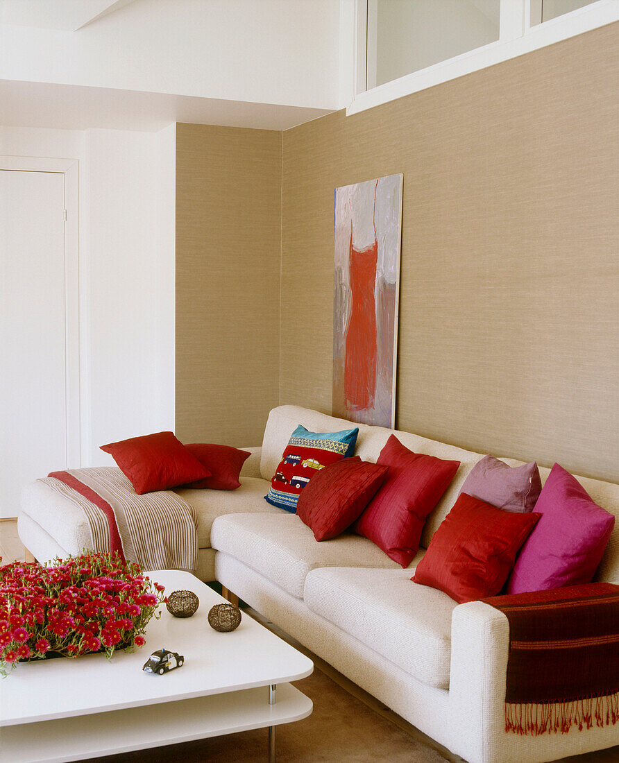 Modernes Wohnzimmer mit einem farbneutralen Sofa mit hellen Kissen und einem niedrigen Tisch mit roten Blumen davor