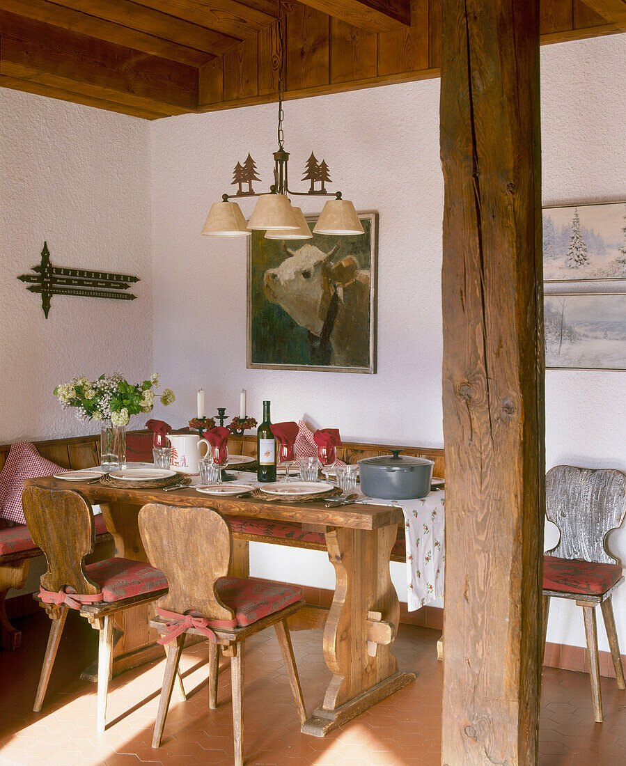 Ein Esszimmer im Landhausstil mit Holzbalken, Holzdecke, Holztisch, Stühlen und Kronleuchter