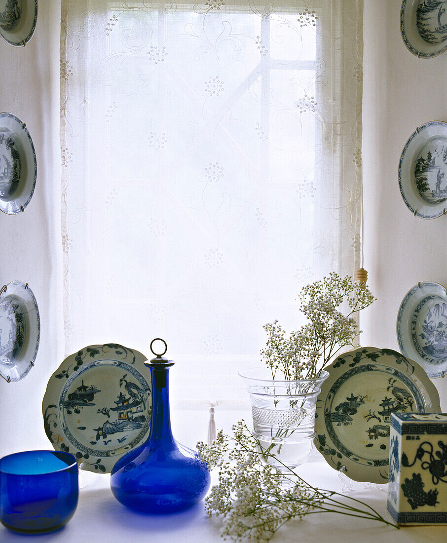 Blaue Glasgefäße, Glasvase und blau-weißes Porzellan auf der Fensterbank