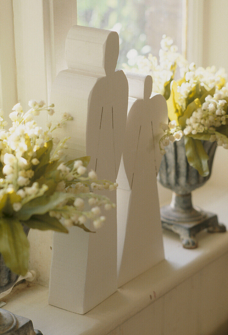 Zwei Holzengel zwischen Pokalsvasen mit weißen Blumen auf Fensterbank