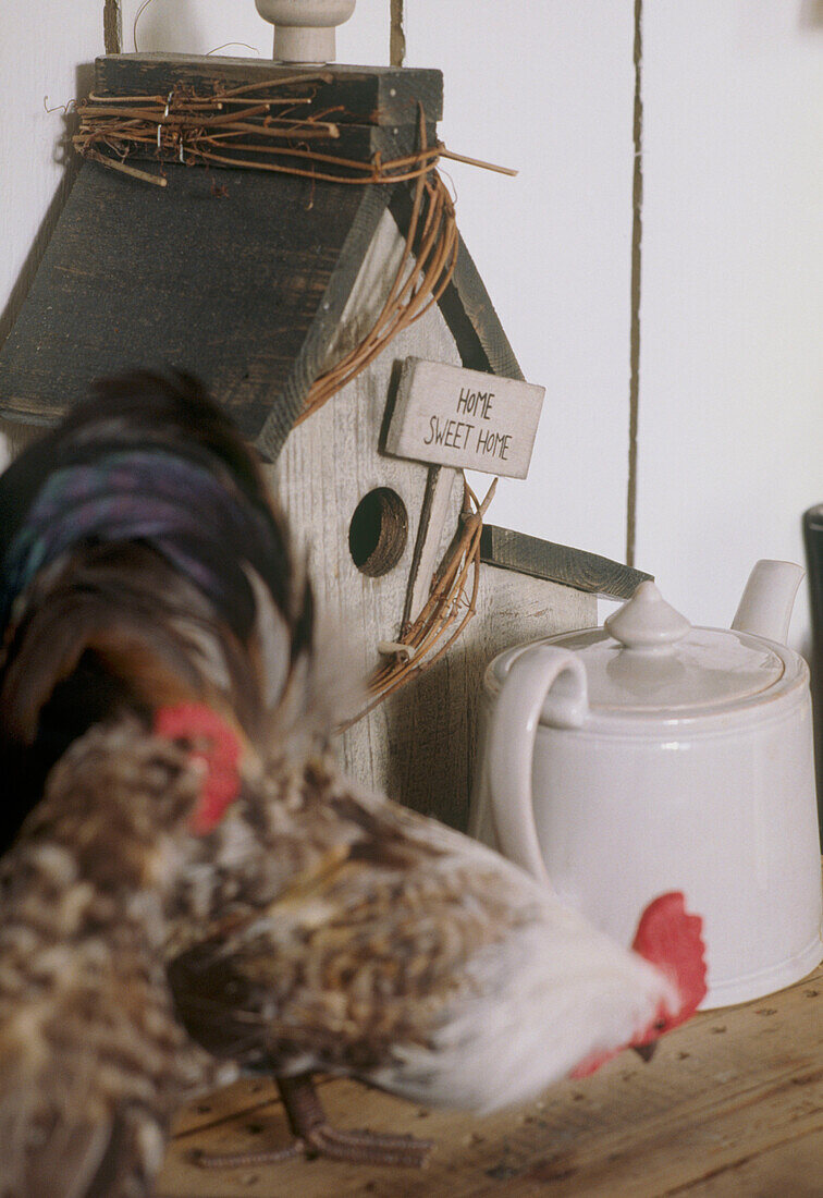 Close up detail of a ornamental birdhouse with on a wooden shelf with two chickens in the foreground