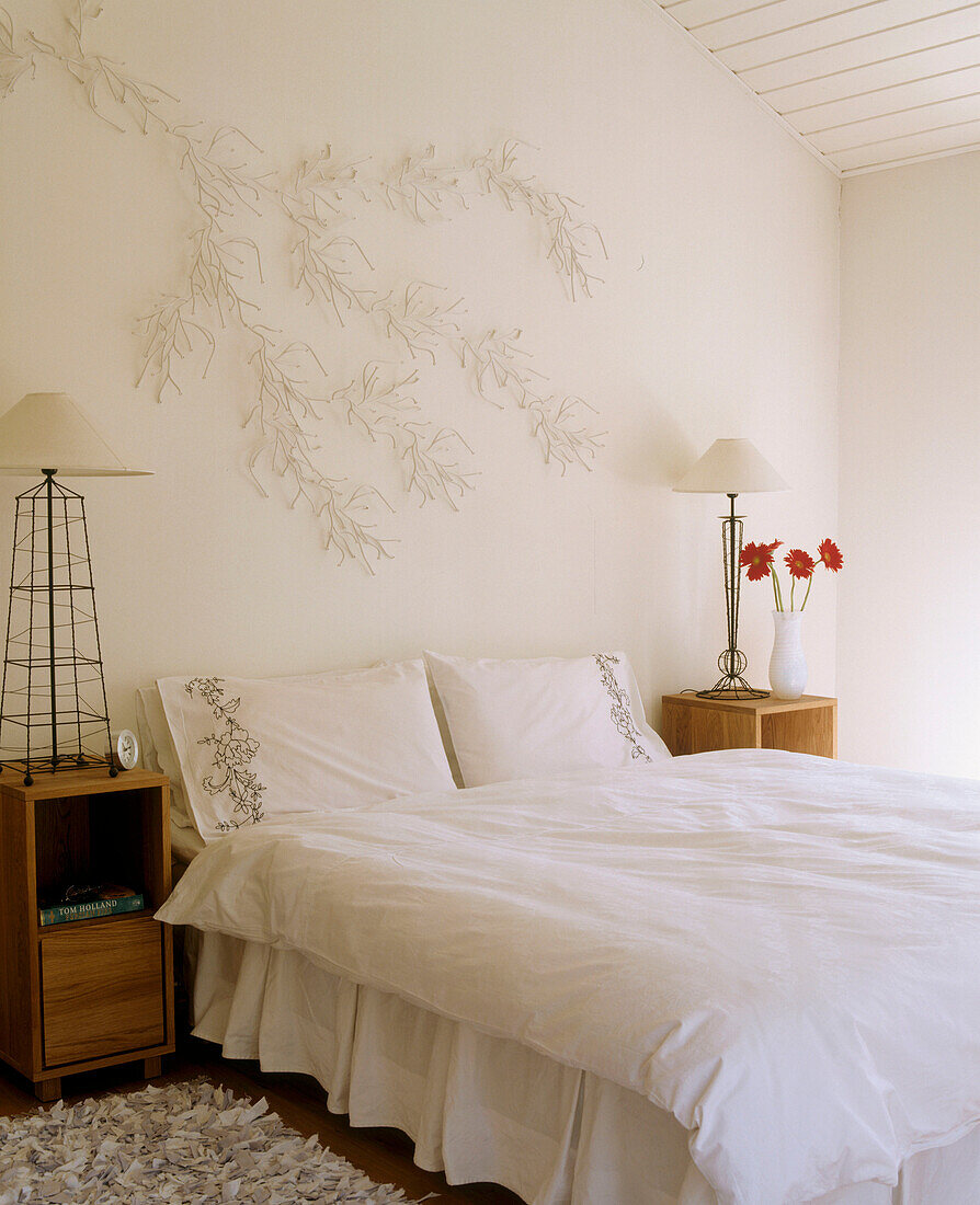 Schlafzimmer mit weißer Bettwäsche und einer dekorativen Leuchte in Form eines Astes über dem Bett