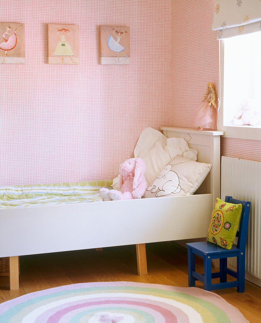 Kinderzimmer mit rosa Wänden und einem bunten Teppich vor einem Bett mit erhöhten Seitenwänden