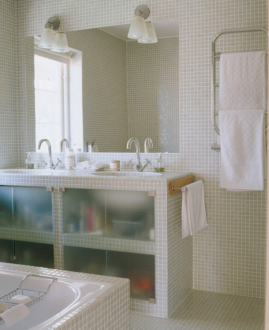Badezimmer mit gefliesten Wänden und einem Spiegel über Waschschrank mit zwei modernen Waschbecken