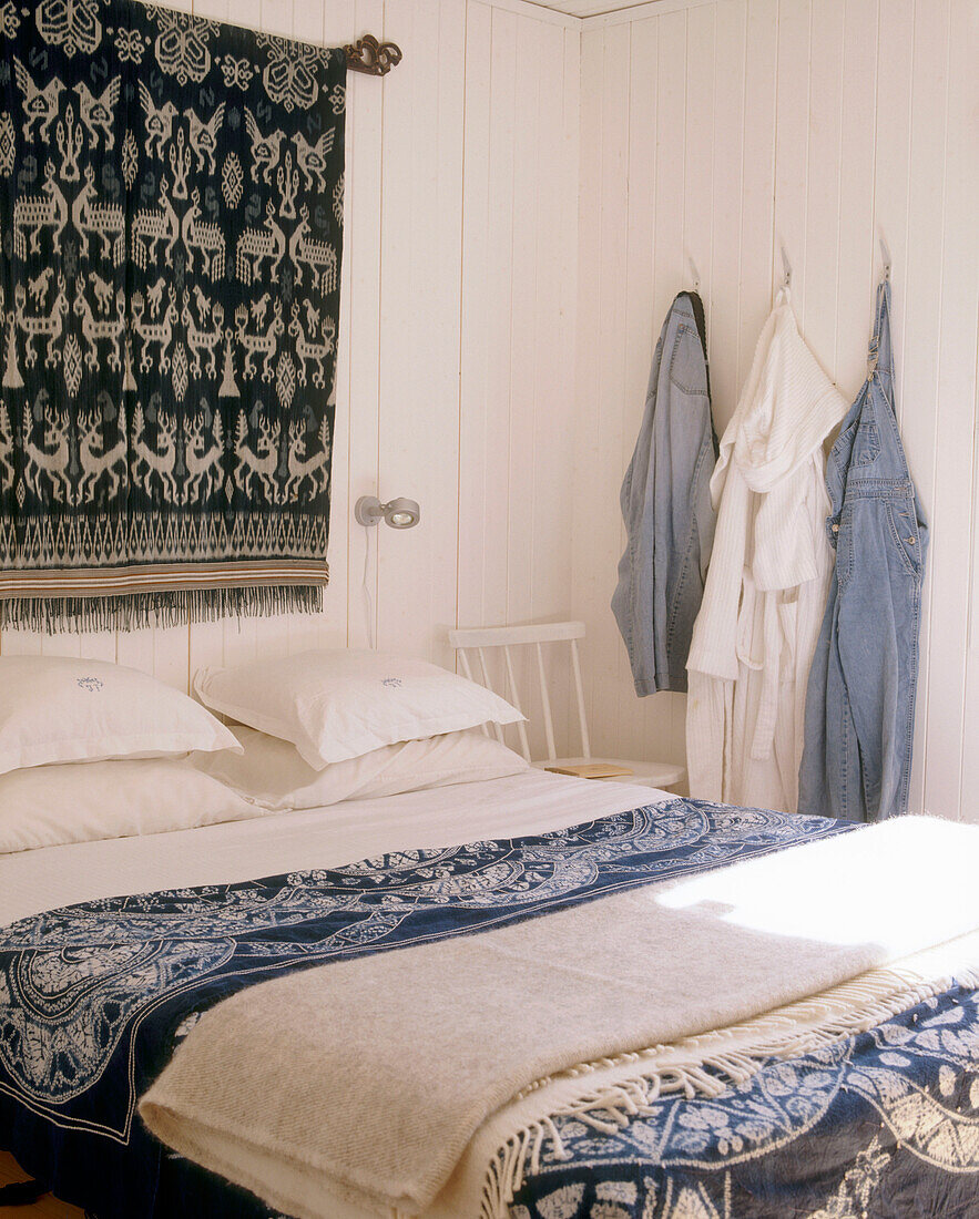 A detail of a traditional bedroom bed with blue and white linen and rug on a wall