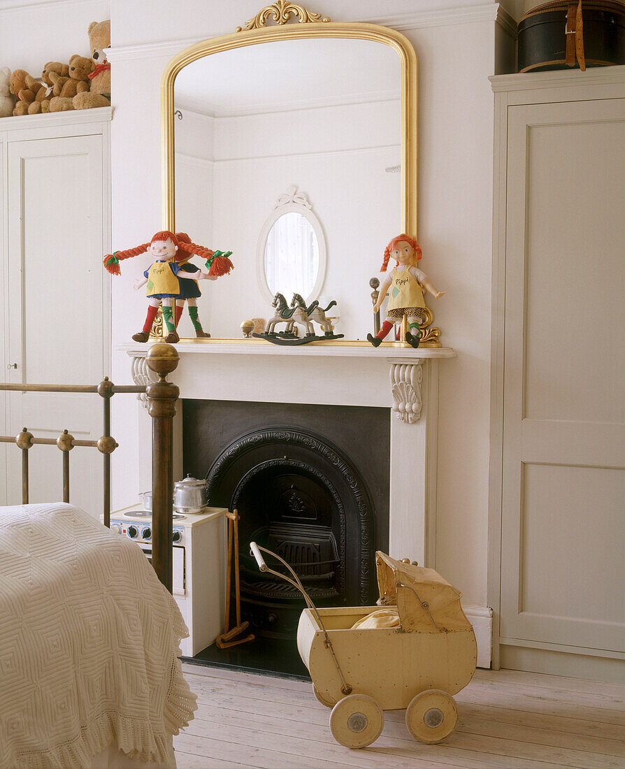 Detail of a gold framed mirror above a traditional fireplace with toys on the mantelpiece in front of a brass framed bed