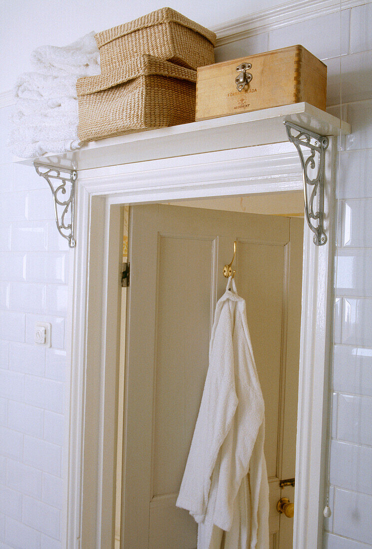 Holzkiste und Weidenkörbe auf weißem Regalbrett über dem Türrahmen