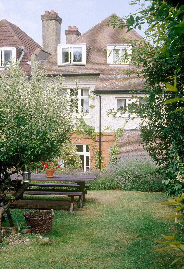 Blick vom Garten mit Rasen und Holzbank auf die Rückseite des Wohnhauses
