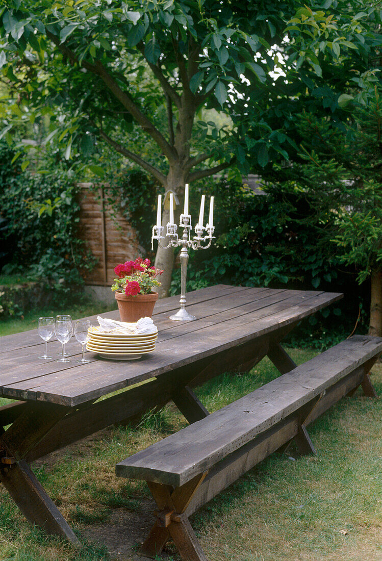 A wooden picnic style table on the lawn displaying a plates and glasses with a candelabra