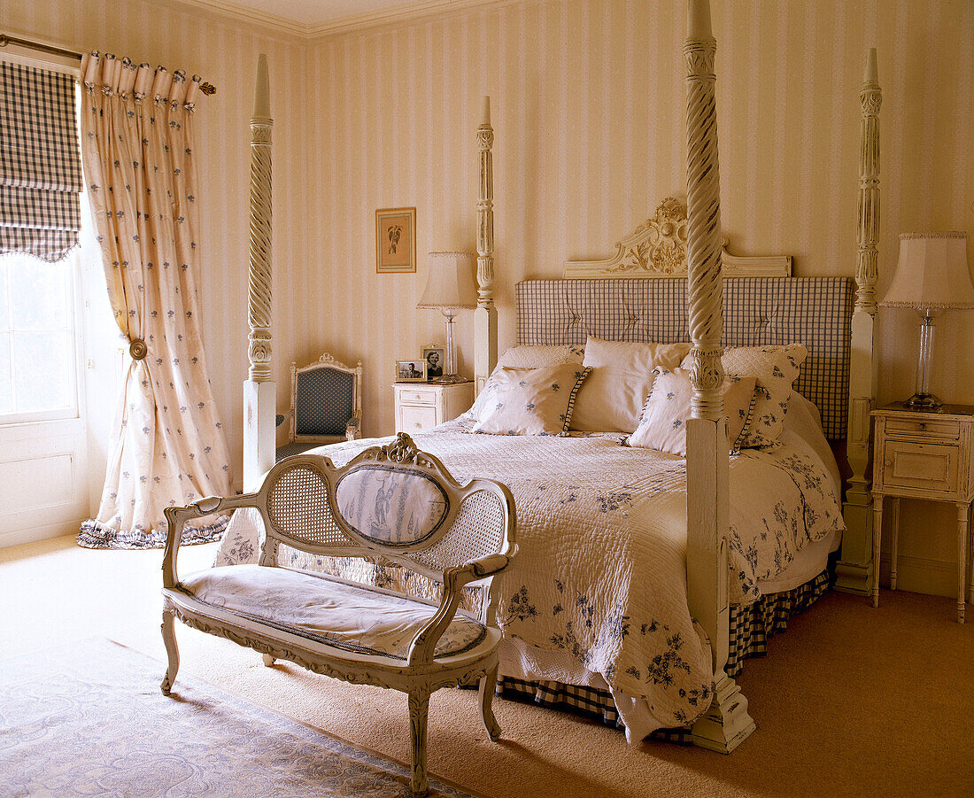 Four poster bed with floral cover in bedroom with settee
