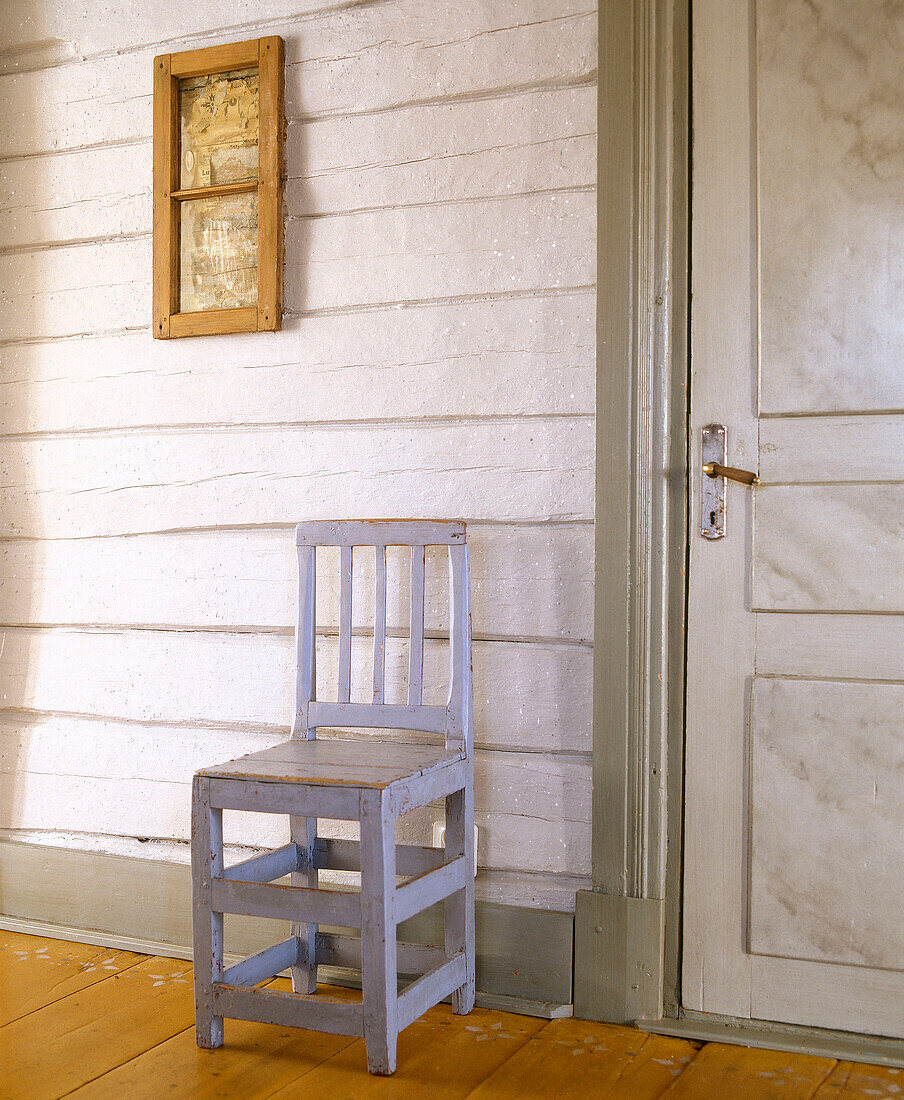 Blau gestrichener Stuhl vor rustikaler holzgetäfelter Wand