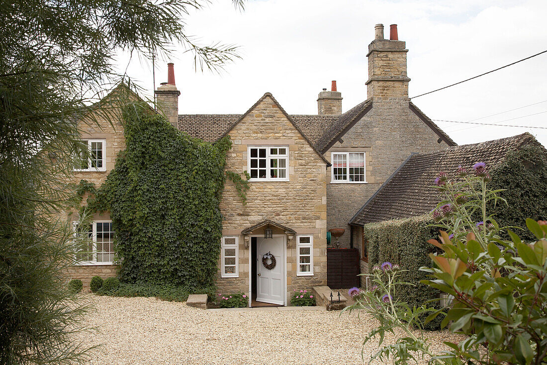 An exterior of a country house with gravel drive shrubs and trees front door open
