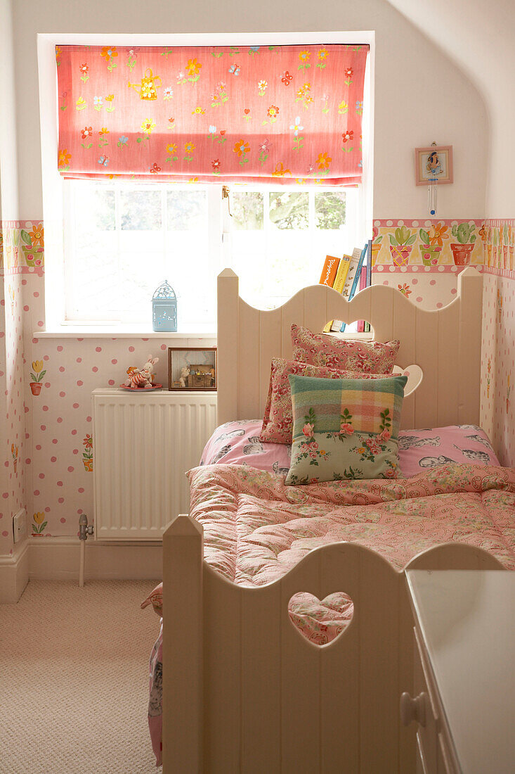 Detail eines in rosa Farben dekorierten Kinderzimmers Einzelbett mit dekorativem hölzernem Kopfteil Raffrollo am Fenster Bettdecke und Tapete mit Blumenmuster
