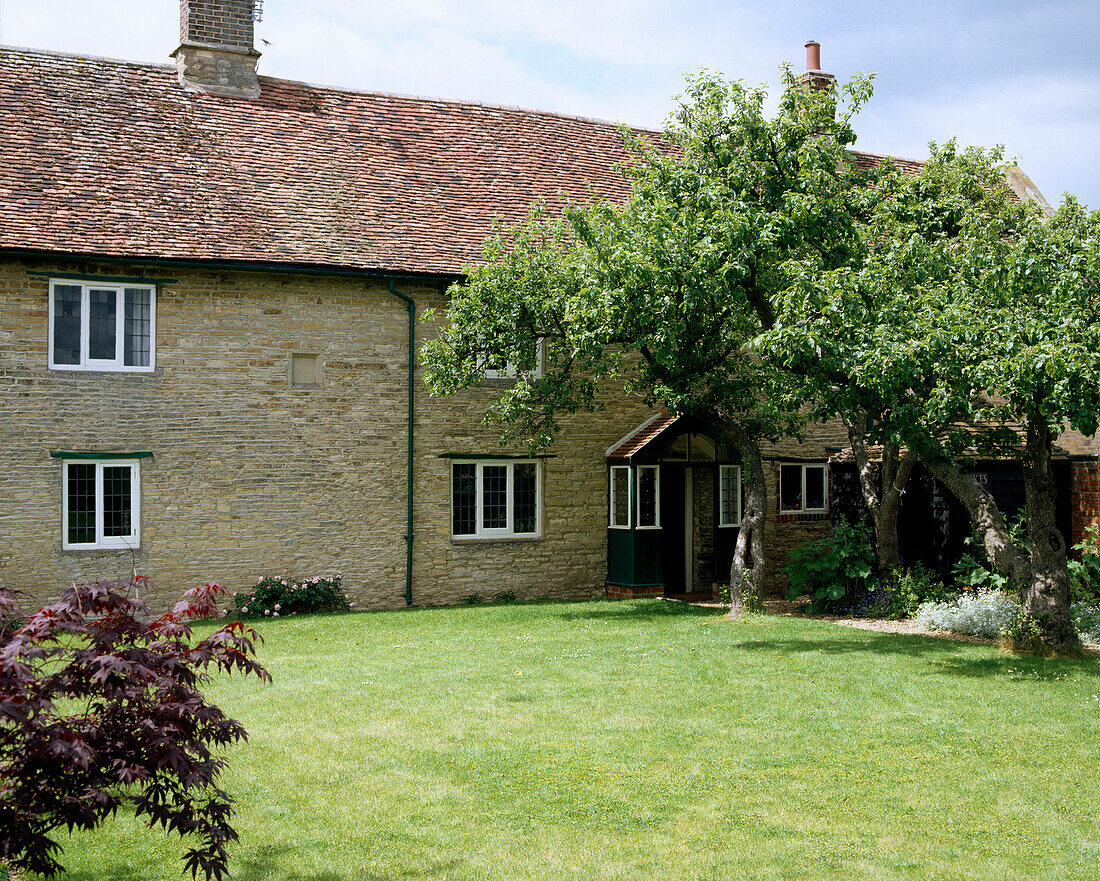 Außenansicht eines englischen Landhauses aus Stein mit Ziegeldach, Vorgarten, Rasen und Bäumen