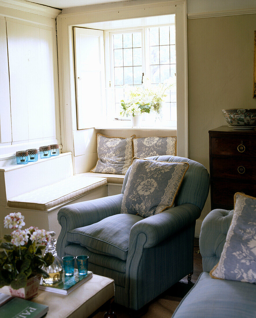 Ein traditionelles Wohnzimmer im Landhausstil mit gepolstertem Sessel, Sitzbank in Fensternische und gemusterten Dekokissen