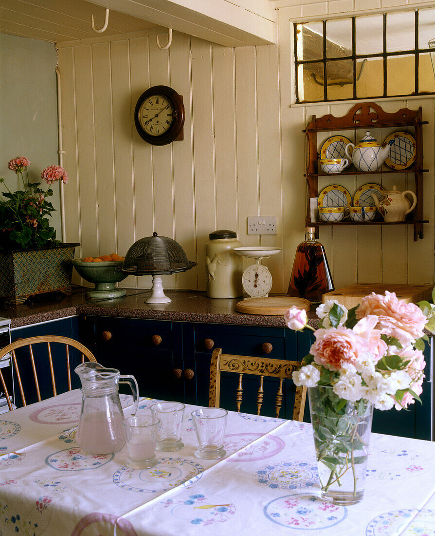 Gelbes Esszimmer im Landhausstil mit gestrichener Holzvertäfelung, Tisch und Holzstühlen, Anrichte, Uhr und Blumenarrangement