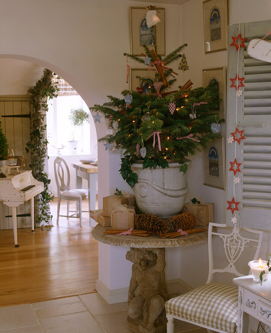 Kleiner geschmückter Weihnachtsbaum in Topf auf Steintisch umgeben von Geschenken und dekorativen Zapfen